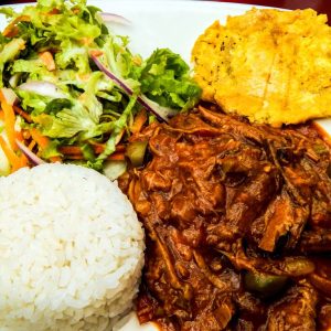 A white plate of Cuban Ropa Vieja, showing tender shredded beef in a vibrant tomato and pepper sauce, next to a side of white rice.